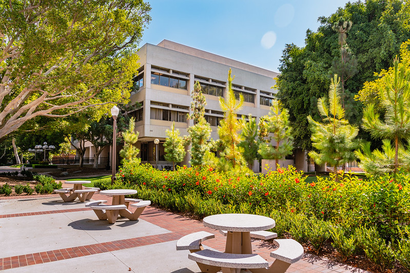 Exterior of gray USC Gould School of Law building surrounded by trees, flowers and tables.