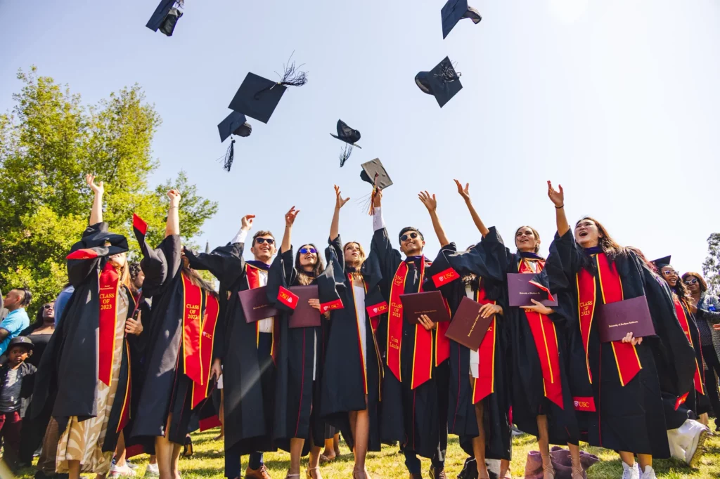 Master of Studies in Law (MSL) graduates wearing gowns at commencement smiling and tossing their caps into the air at their graduation celebration.