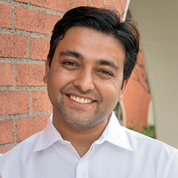 Photo of LLM in ADR graduate Rohit Adlakha smiling in a white shirt in front of a brick building
