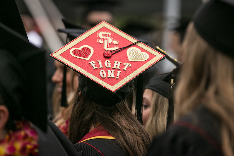 Woman sitting at graduation wearing black robes and a USC-decorated mortarboard.