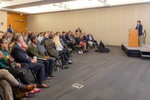 A man at a podium speaks to a seated audience